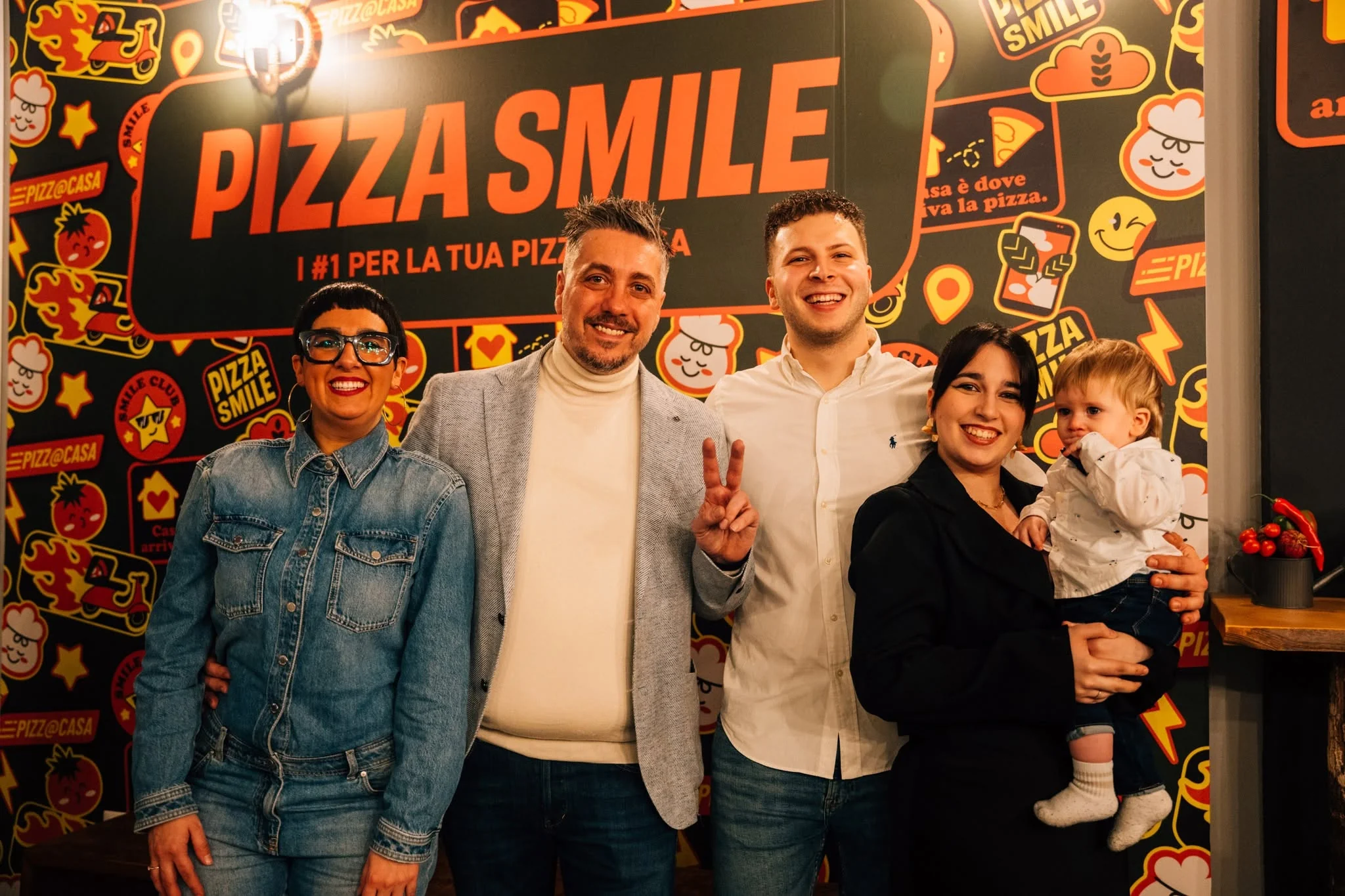 Persone sorridenti e un bambino davanti al muro Pizza Smile nel negozio di Cavarzere.