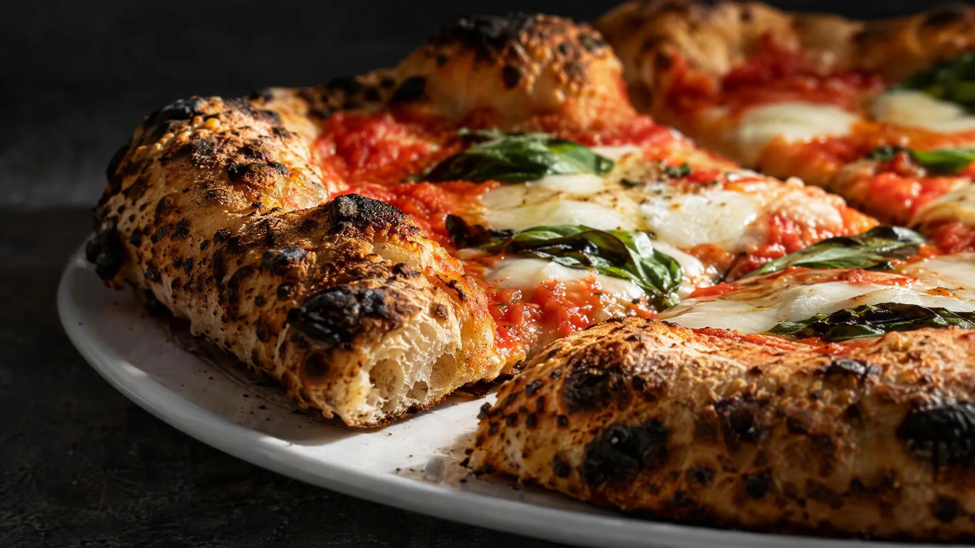 Cornicione alveolato e croccante di una pizza margherita a spicchi su un piatto bianco